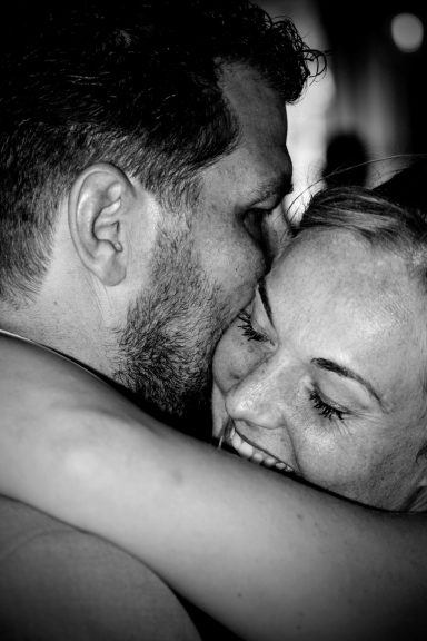 Een man en vrouw omhelzen elkaar lachend in een intieme, zwart-wit foto.