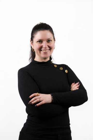 Vrouw in zwarte trui staat met de armen gekruist en glimlacht.