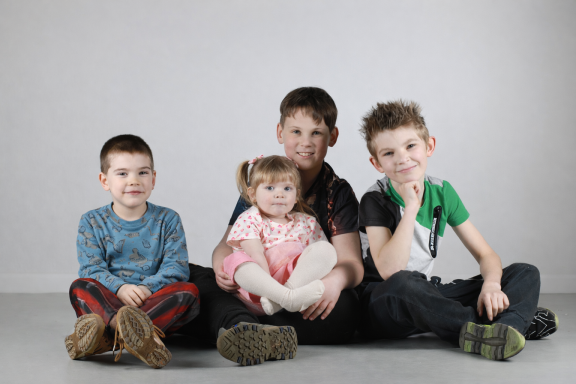Vier kinderen zitten samen op de grond, met een neutrale achtergrond.