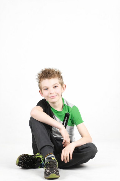 Jongentje met een groene shirt en spijkerbroek, zittend op de grond met een glimlach.